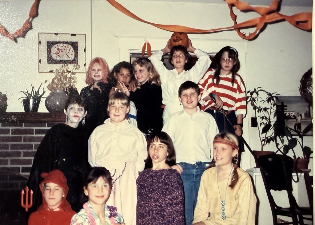 A dozen people in Halloween costume by the fireplace.