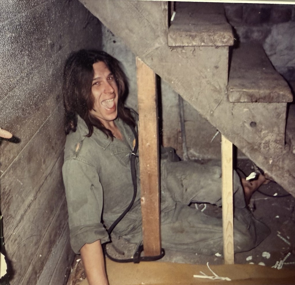 A person grinning under the open basement stairs.