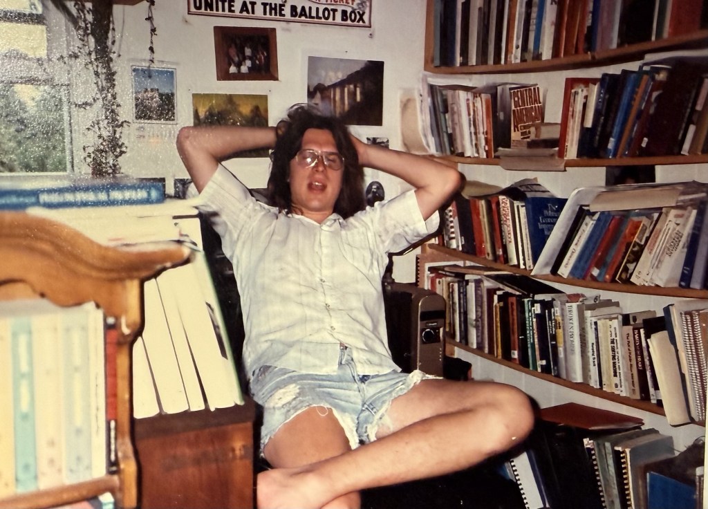 A person reclining against bookshelves below a UNITE AT THE BALLOT BOX poster.