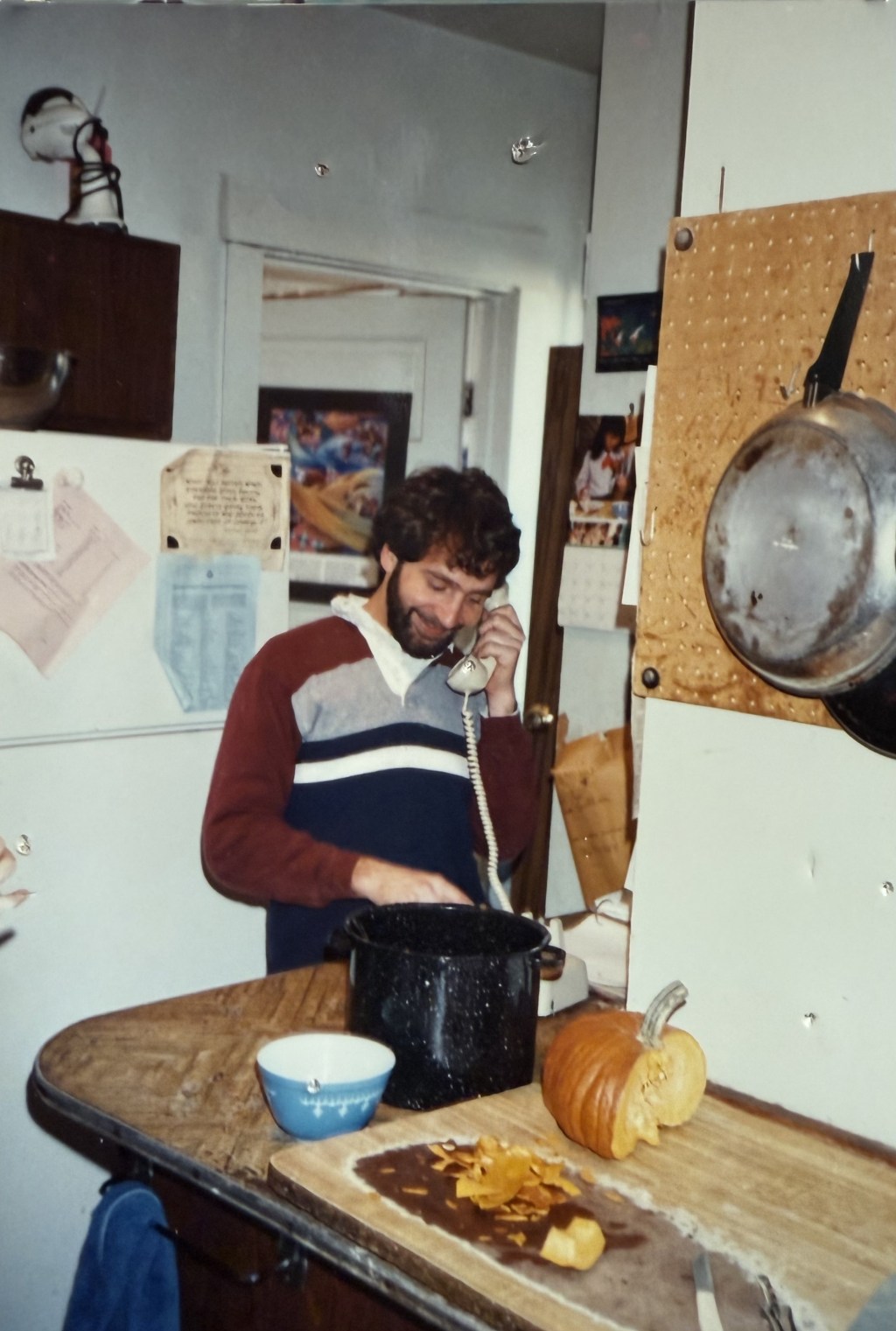 A man on the wall phone stirring a stockpot.