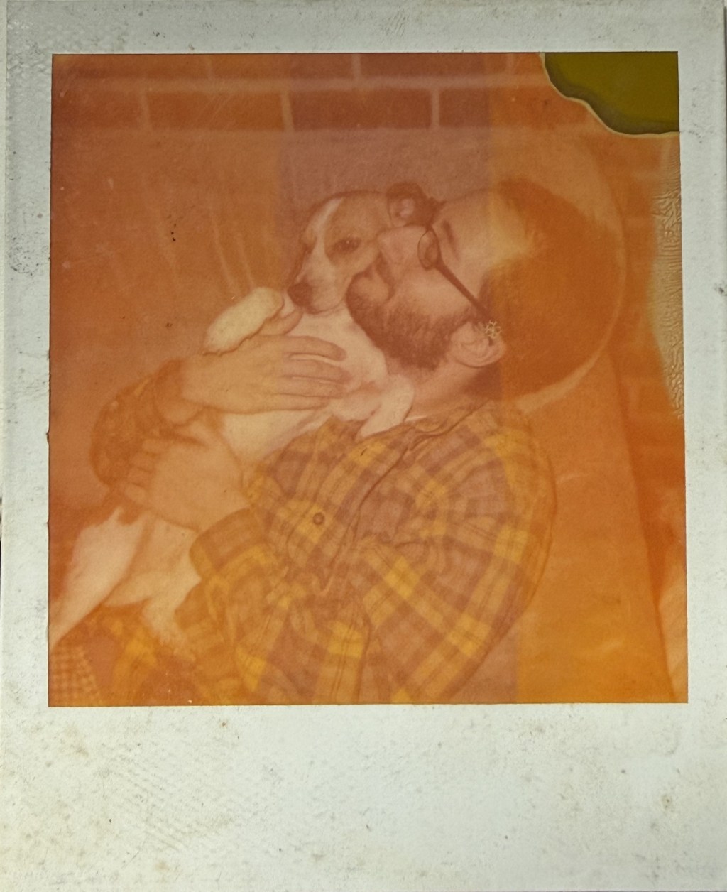 Orange-cast Polaroid of a bearded man holding a dog.